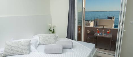 A hotel room with a bed, a small table with drinks, and a balcony with a view of the sea.