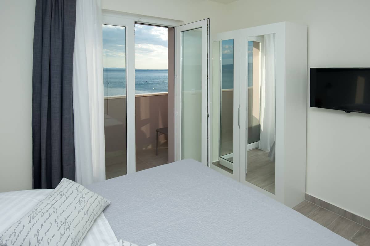 A hotel room with a bed, a TV, a balcony with a view of the sea, and a sliding glass door.