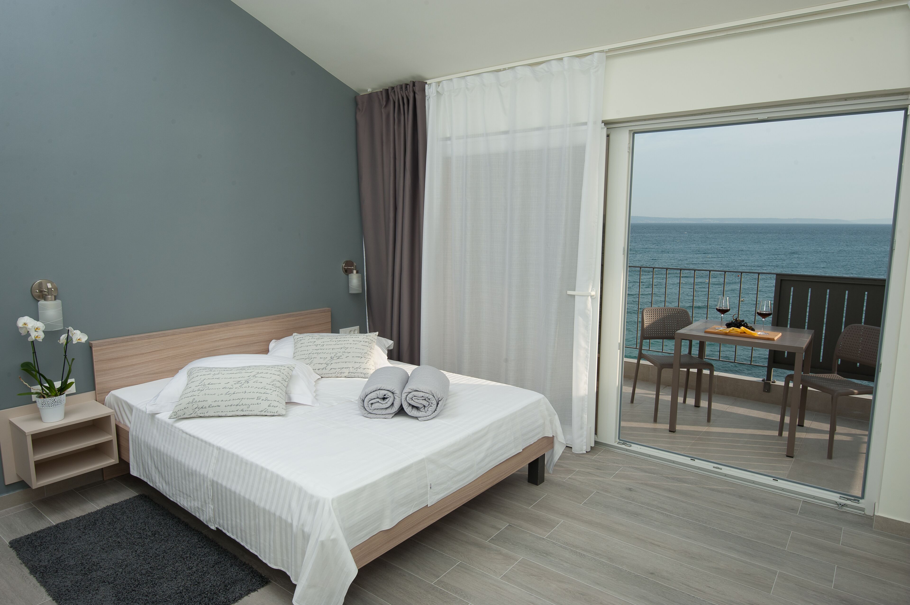 A hotel room with a bed, a small table, and a balcony with a view of the sea.