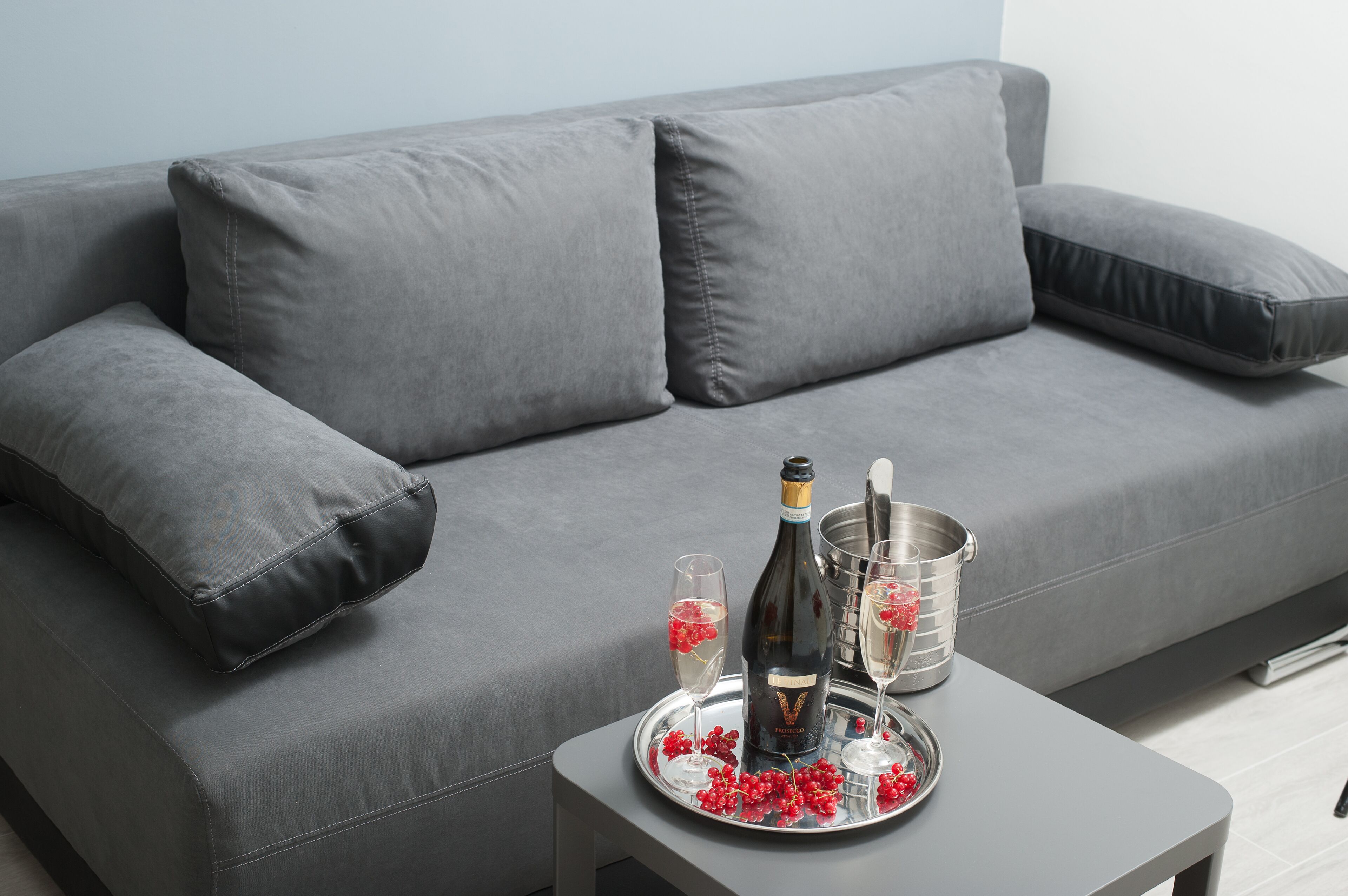 A grey sofa with two cushions, a tray with a bottle, glasses, and red berries.
