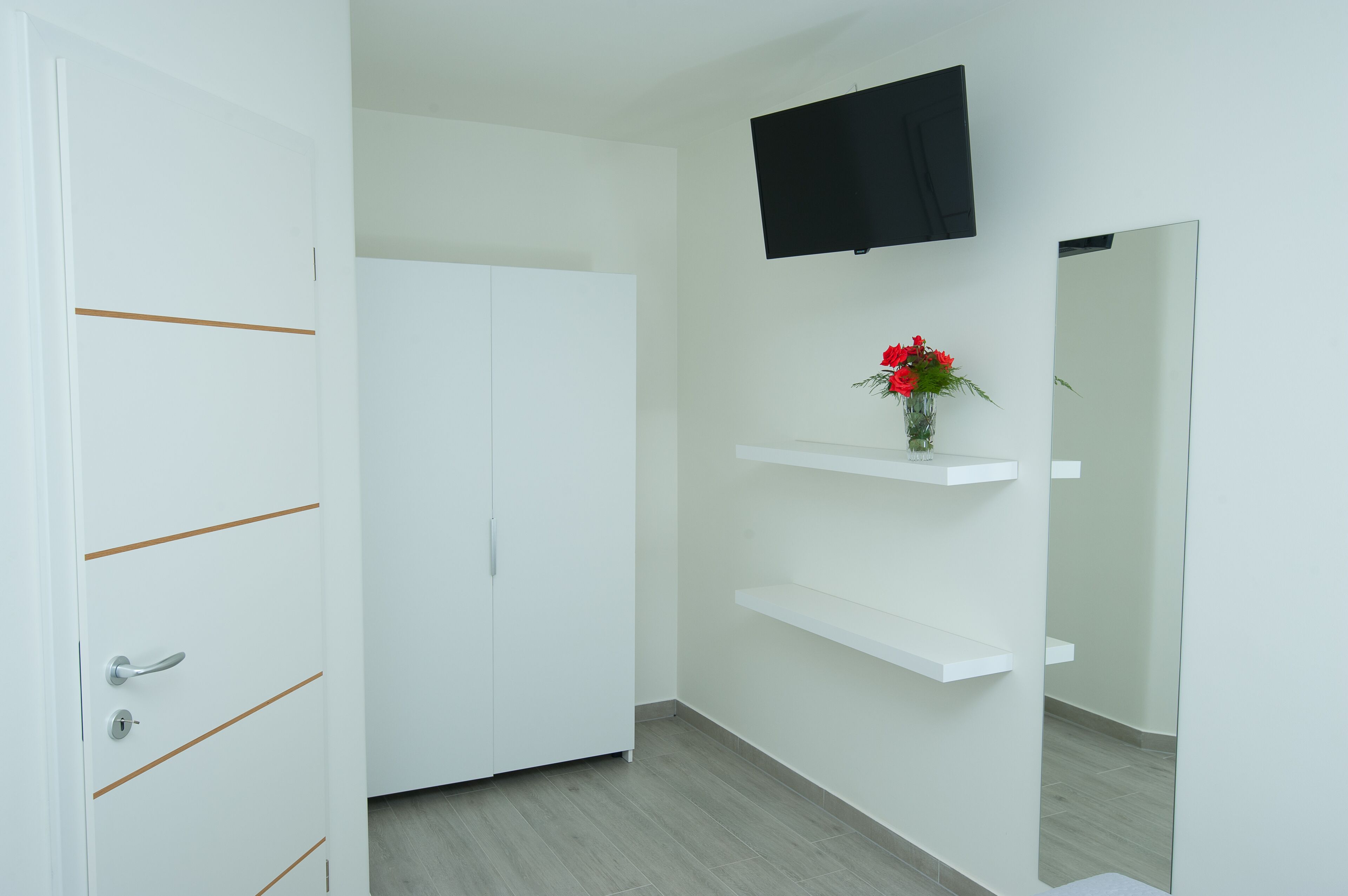 A white room with a wardrobe, a mounted TV, and a mirror.