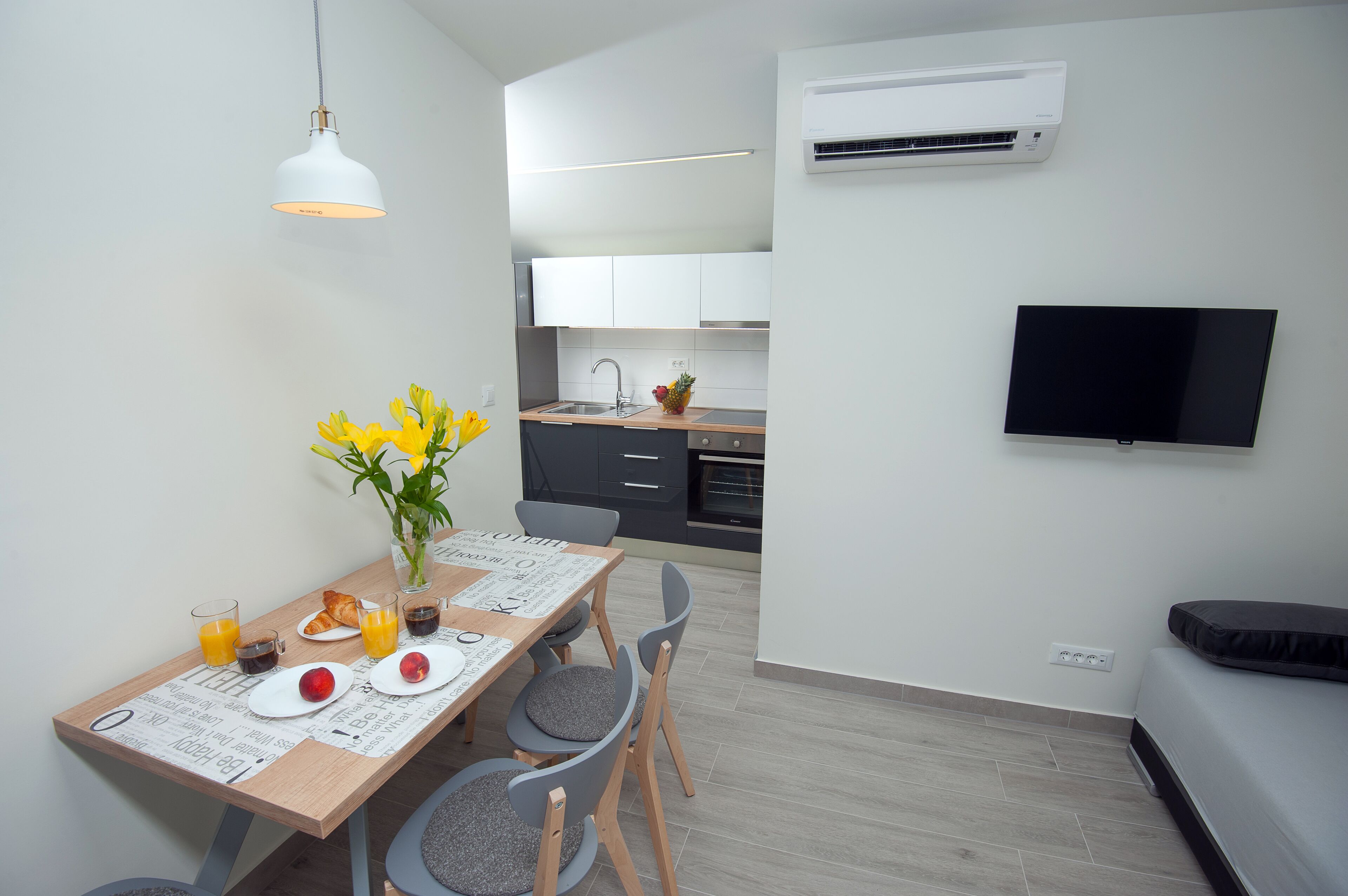 A modern kitchen with white cabinets, a flat-screen TV, and a dining area with a wooden table and chairs.