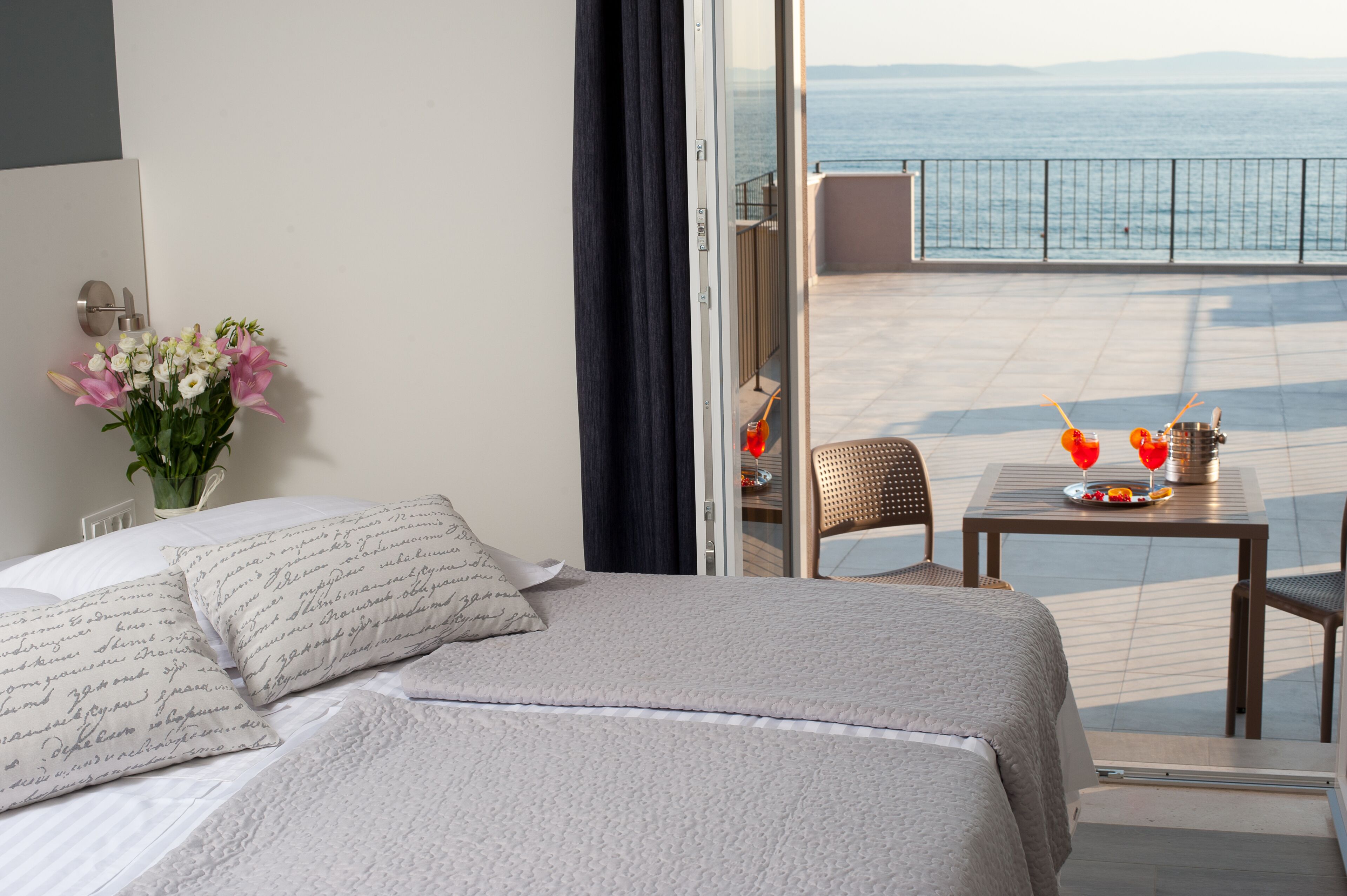 Ein Hotelzimmer mit Bett, einem kleinen Tisch mit einem Getränk und Blick aufs Meer.