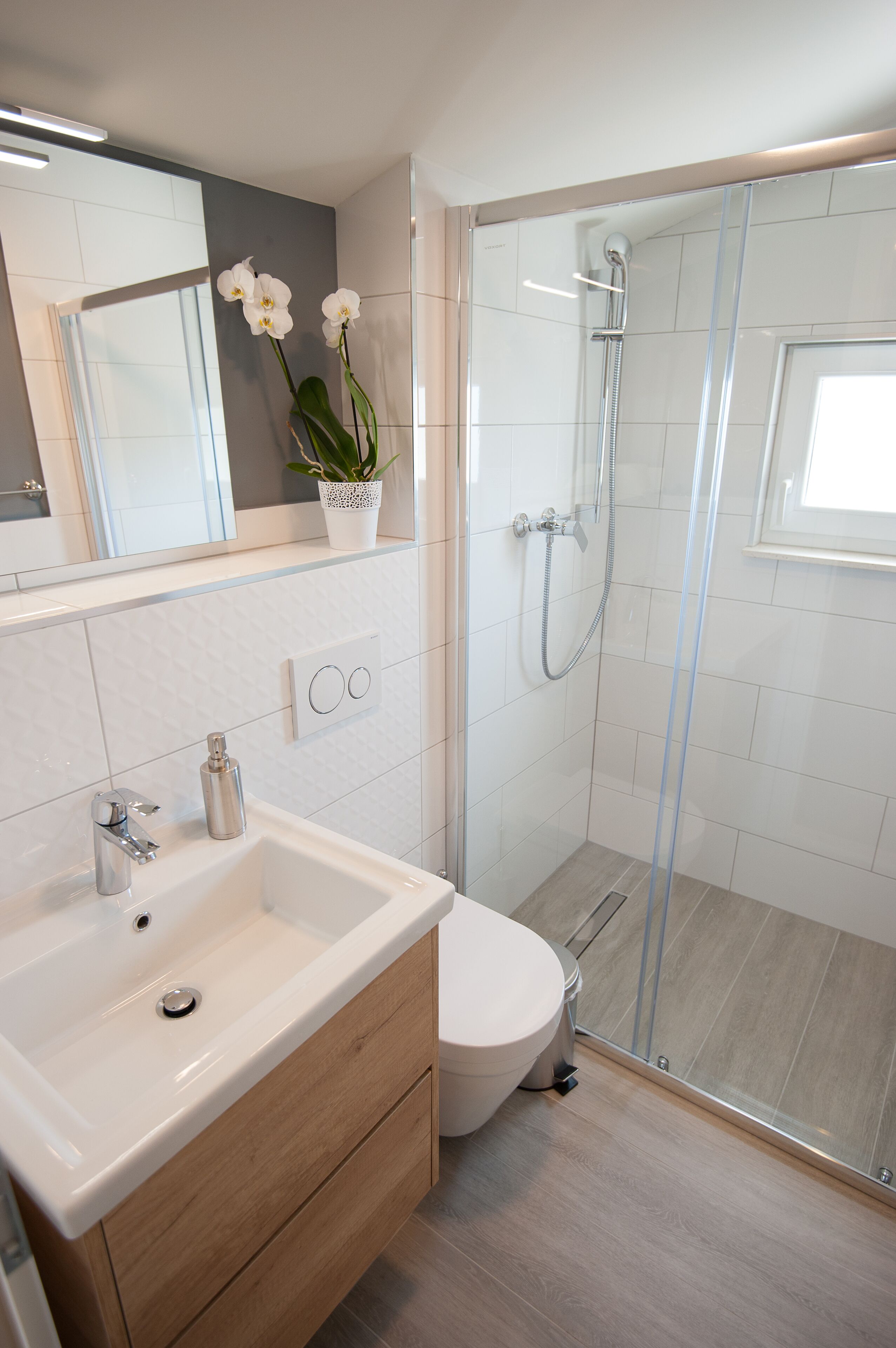 A modern bathroom with a glass-enclosed shower, a white sink, and a toilet.