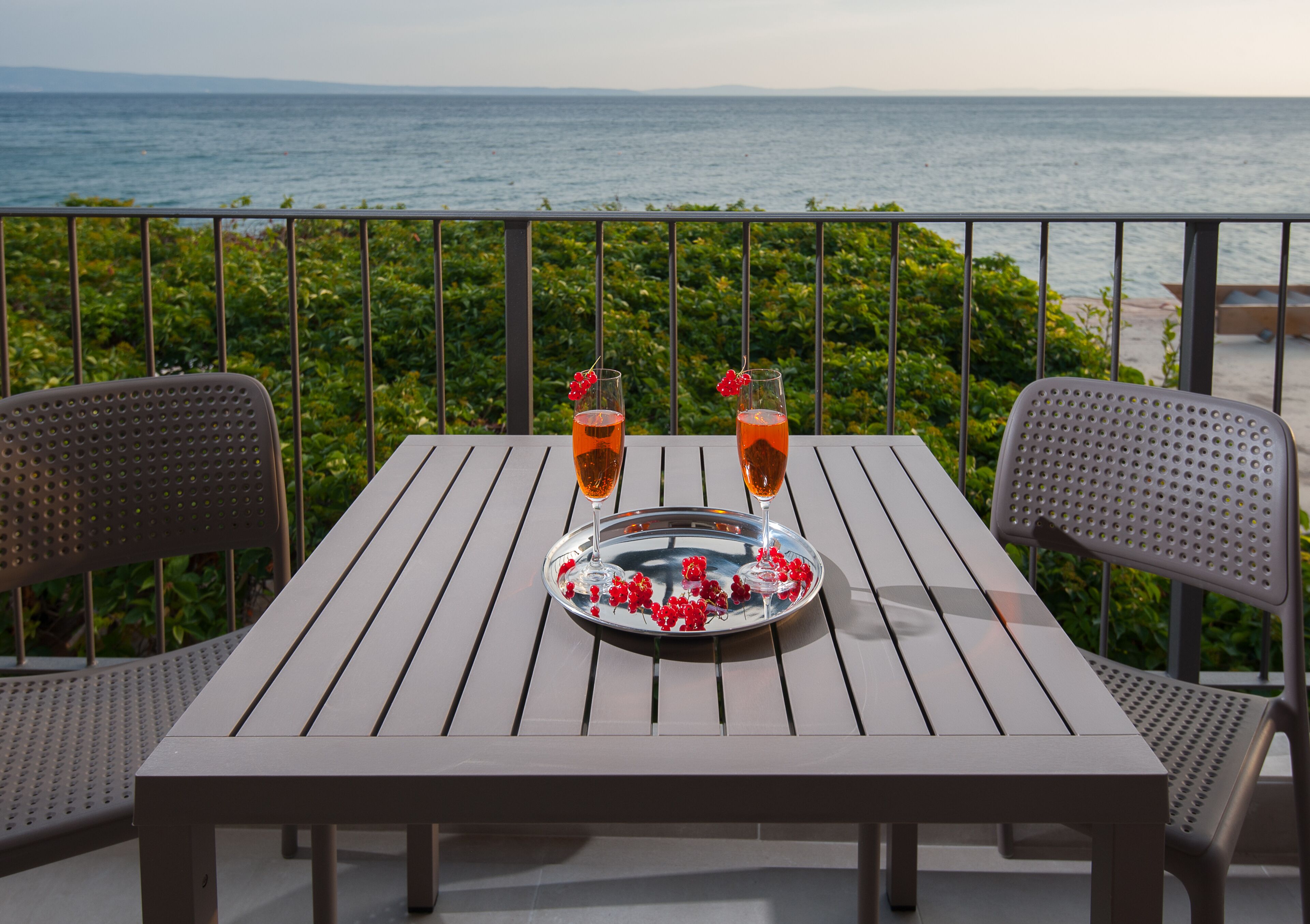 Ein Tisch mit zwei Gläsern, ein Tablett mit roten Blumen und Blick auf das Meer.
