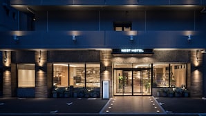 A hotel entrance with a modern design, featuring a prominent sign, large windows, and potted plants. - Nest Hotel Hakata Station (Fukuoka)