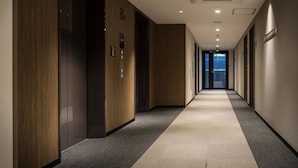 A long, narrow hallway with wooden paneling on the walls, carpeted floors, and a series of doors on one side. - Nest Hotel Hakata Station (Fukuoka)