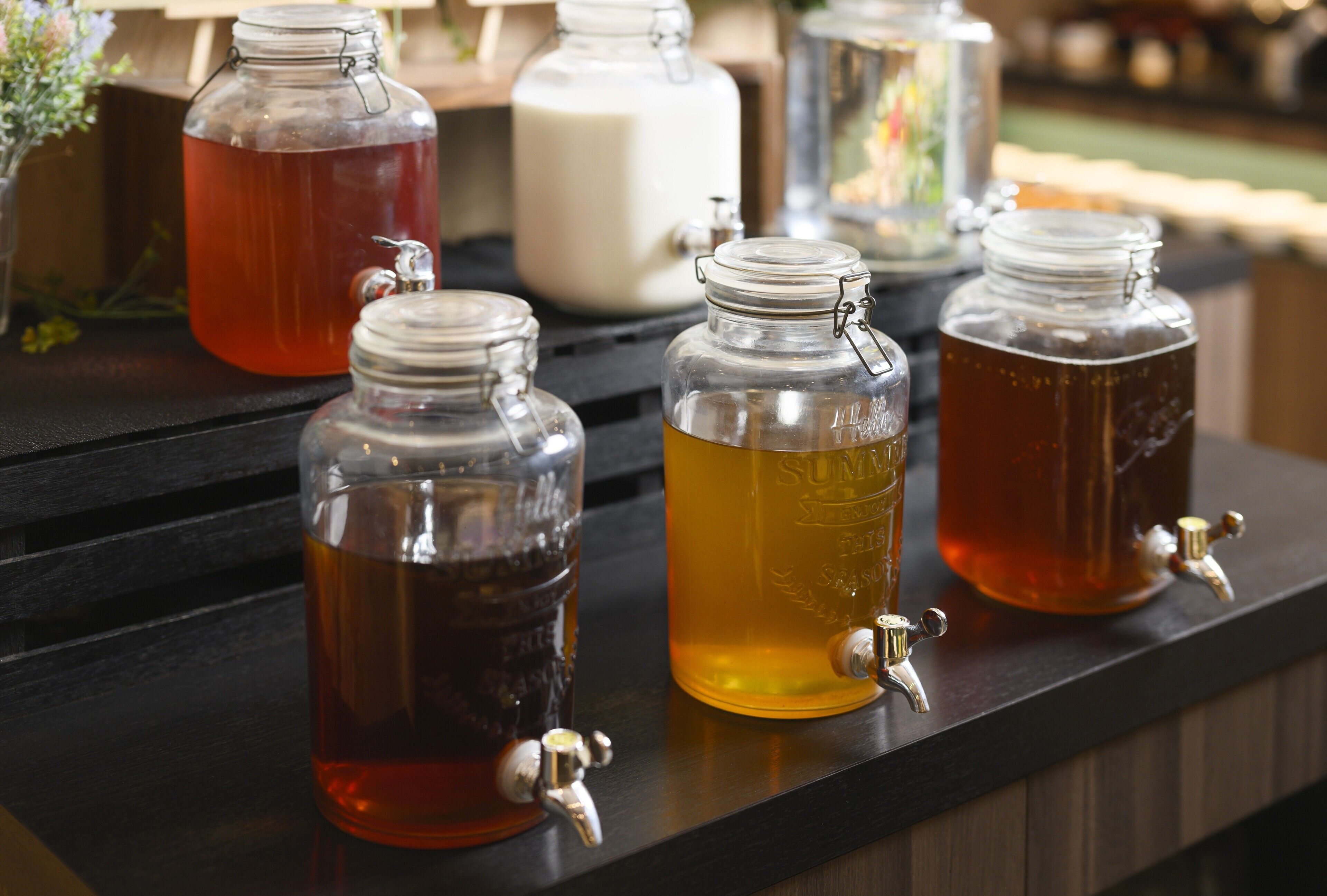 Four glass jars with taps on a wooden counter, likely containing beverages.