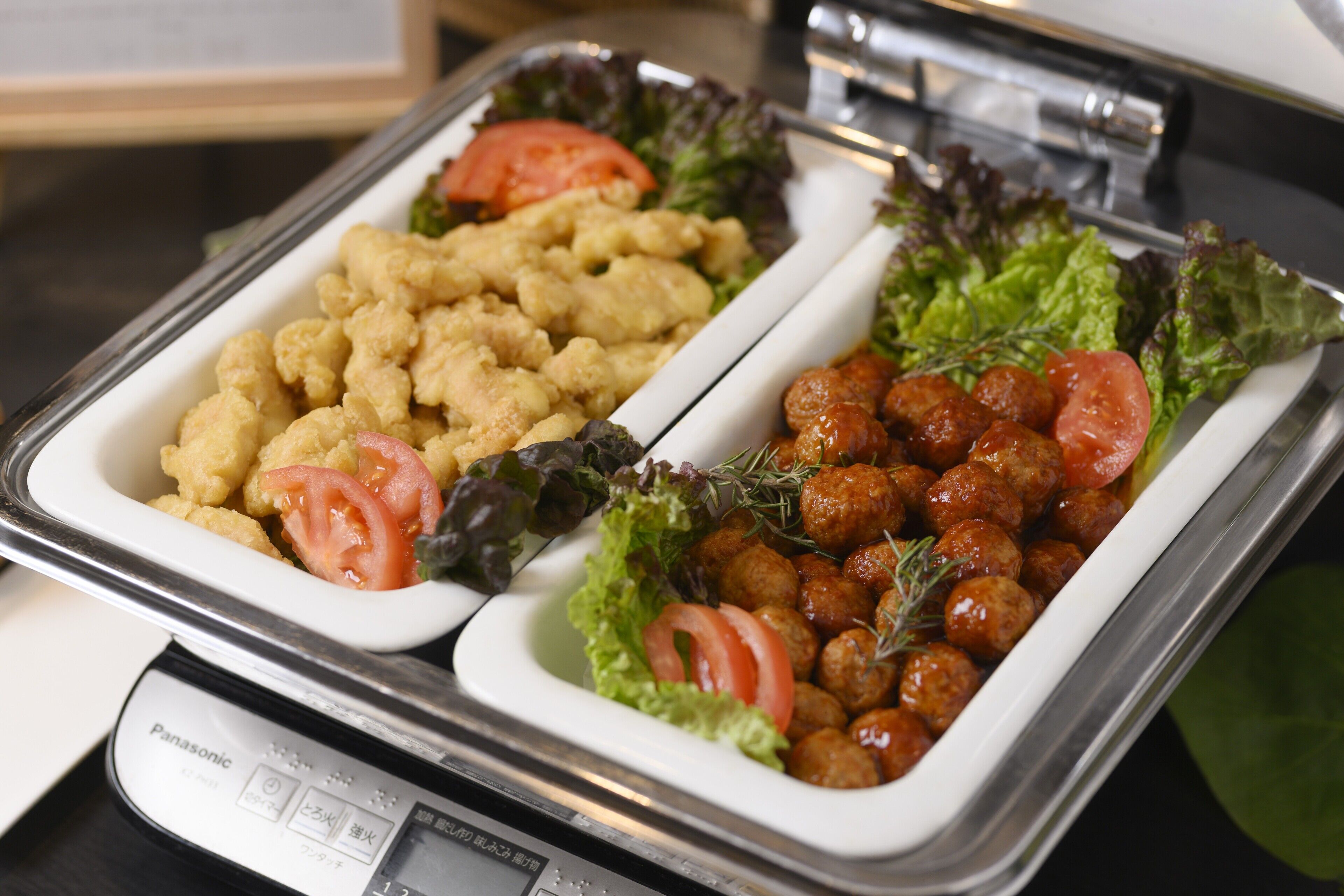 A buffet with two trays of food, one with breaded items and the other with meatballs, both garnished with lettuce and tomatoes.