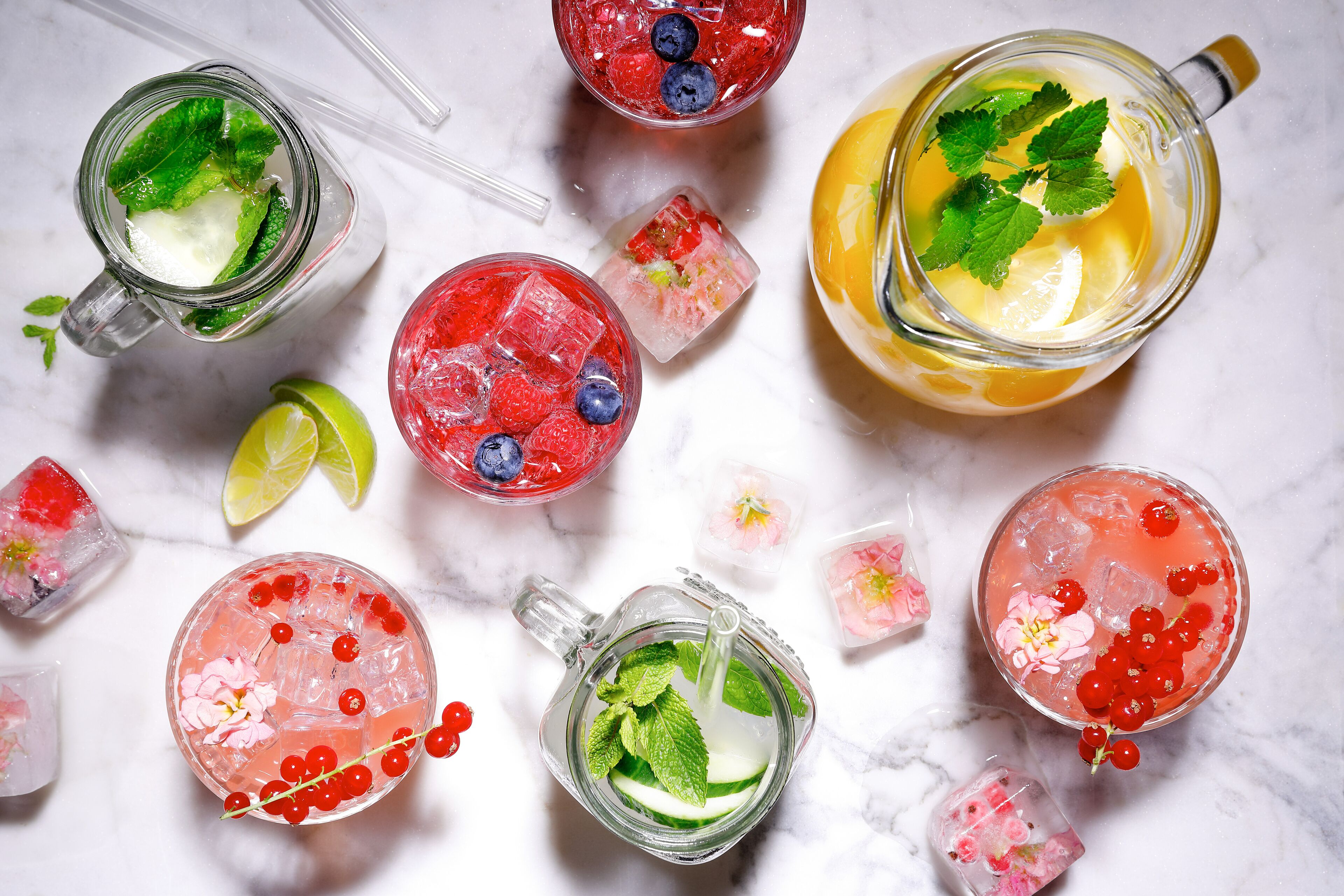 Various drinks with ice and garnishes on a marble surface.
