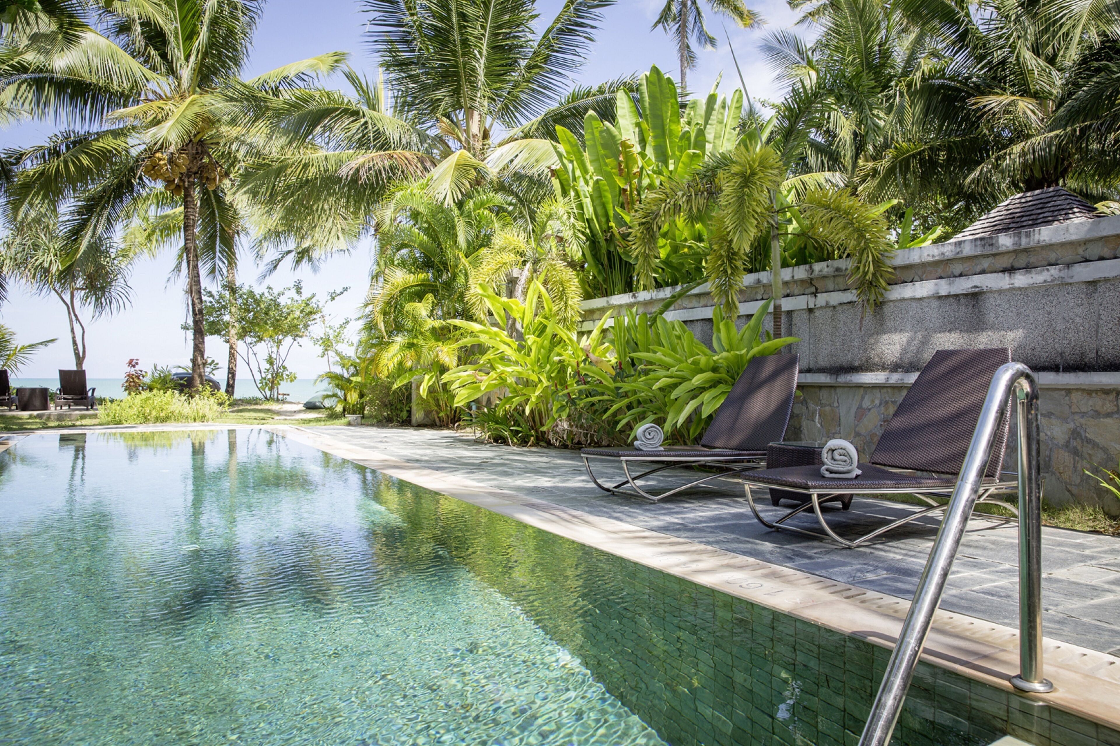 A clear pool with lounge chairs and palm trees.