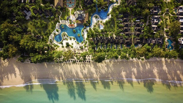 Vista aérea de un complejo turístico con varias piscinas, acceso a la playa y densa vegetación tropical.