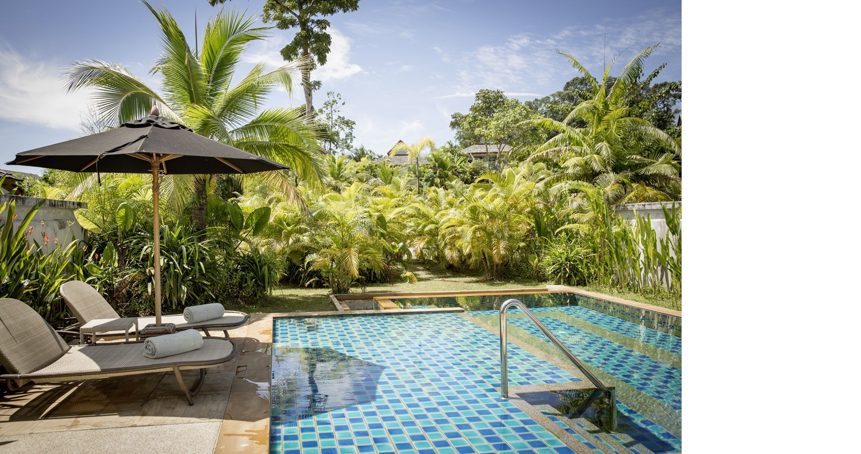 Una piscina con sillas de descanso y una sombrilla, rodeada de exuberante vegetación.
