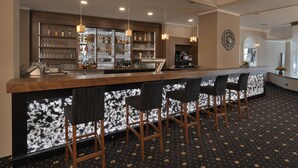 A bar area with a wooden counter, bar stools, and shelves stocked with bottles and glasses. - Hotel Am Schloss Aurich (Aurich)