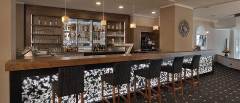 A bar area with a wooden counter, bar stools, and shelves stocked with bottles and glasses.