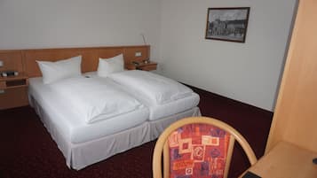 A hotel room with a double bed, a wooden headboard, a nightstand, a chair, a desk, and a framed picture on the wall.