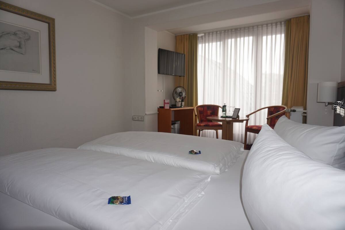 Une chambre d’hôtel avec deux lits, un bureau, une chaise et un téléviseur fixé au mur.