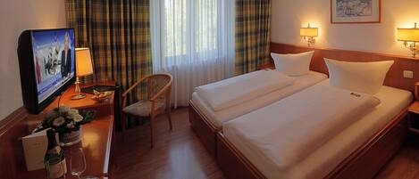 A hotel room with two beds, a television, a desk with a lamp, a chair, and a window with curtains.