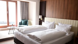 A hotel room with a large bed, a small round table, a chair, and a window with curtains. - Hotel Am Schloss Aurich (Aurich)