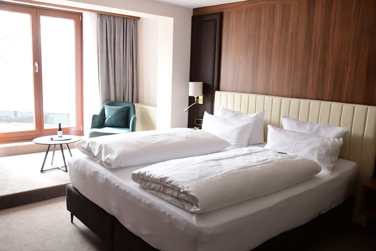 Une chambre d’hôtel avec un grand lit, une petite table ronde, une chaise et une fenêtre avec des rideaux.