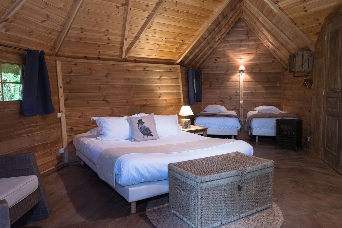 A cozy log cabin bedroom with a loft-style bed, a nightstand with a lamp, and a wicker chest.