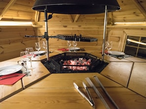 A wooden dining table with a built-in grill, surrounded by wine glasses and plates. - Domaine de la Boulaie (Treize-Vents)