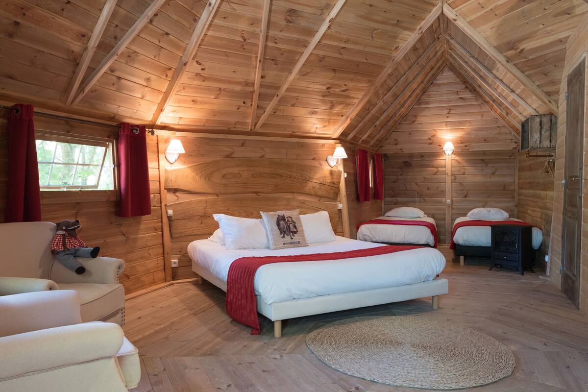 A cozy log cabin bedroom with two beds, a sofa, and a teddy bear.