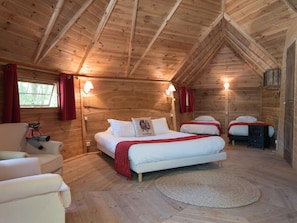 A cozy log cabin bedroom with two beds, a sofa, and a teddy bear. - Domaine de la Boulaie (Treize-Vents)