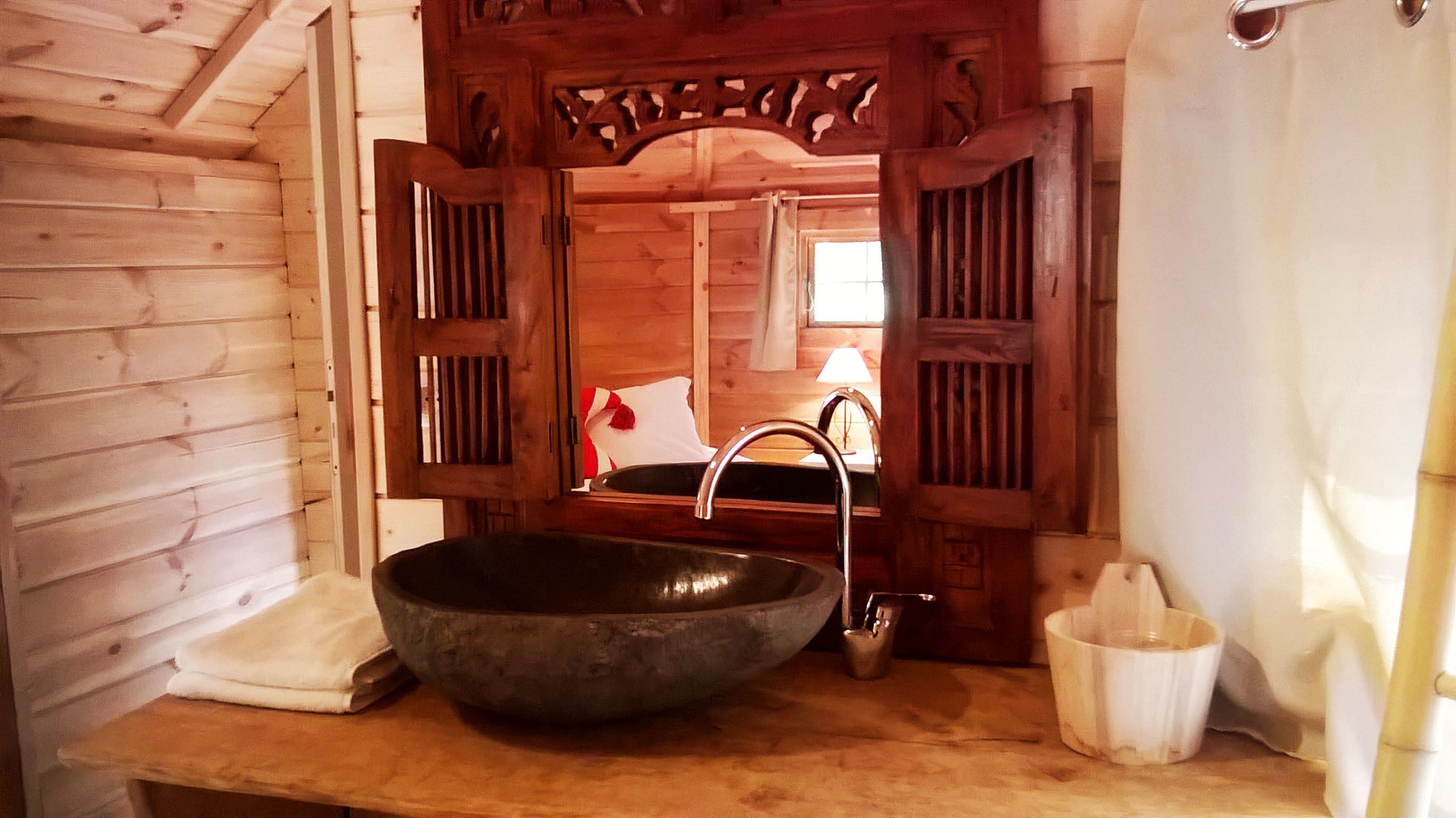 L’intérieur d’un chalet rustique en bois, avec un grand lavabo noir, une porte en bois ornée de sculptures complexes et une petite fenêtre agrémentée d’un rideau blanc.