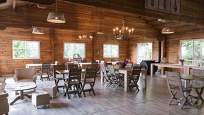 A spacious dining area with wooden walls and multiple windows, featuring a chandelier and a rustic fireplace. - Domaine de la Boulaie (Treize-Vents)