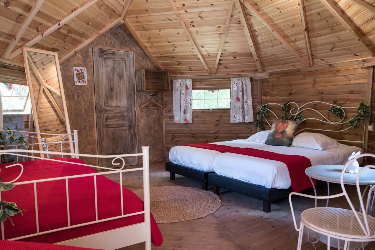 A cozy cabin-style bedroom with a large bed, a smaller bed, and a single chair.