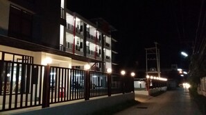 A multi-story building with balconies, a gated entrance, and a street with parked cars. - KP Place (Lop Buri)
