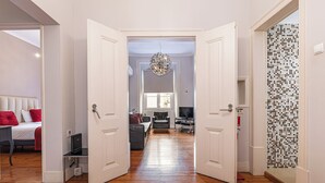 En hall leder till ett sovrum med en säng, ett skrivbord och en stol. På höger sida finns en dörr som leder till ett annat rum med en vägg som är klädd med kakel.