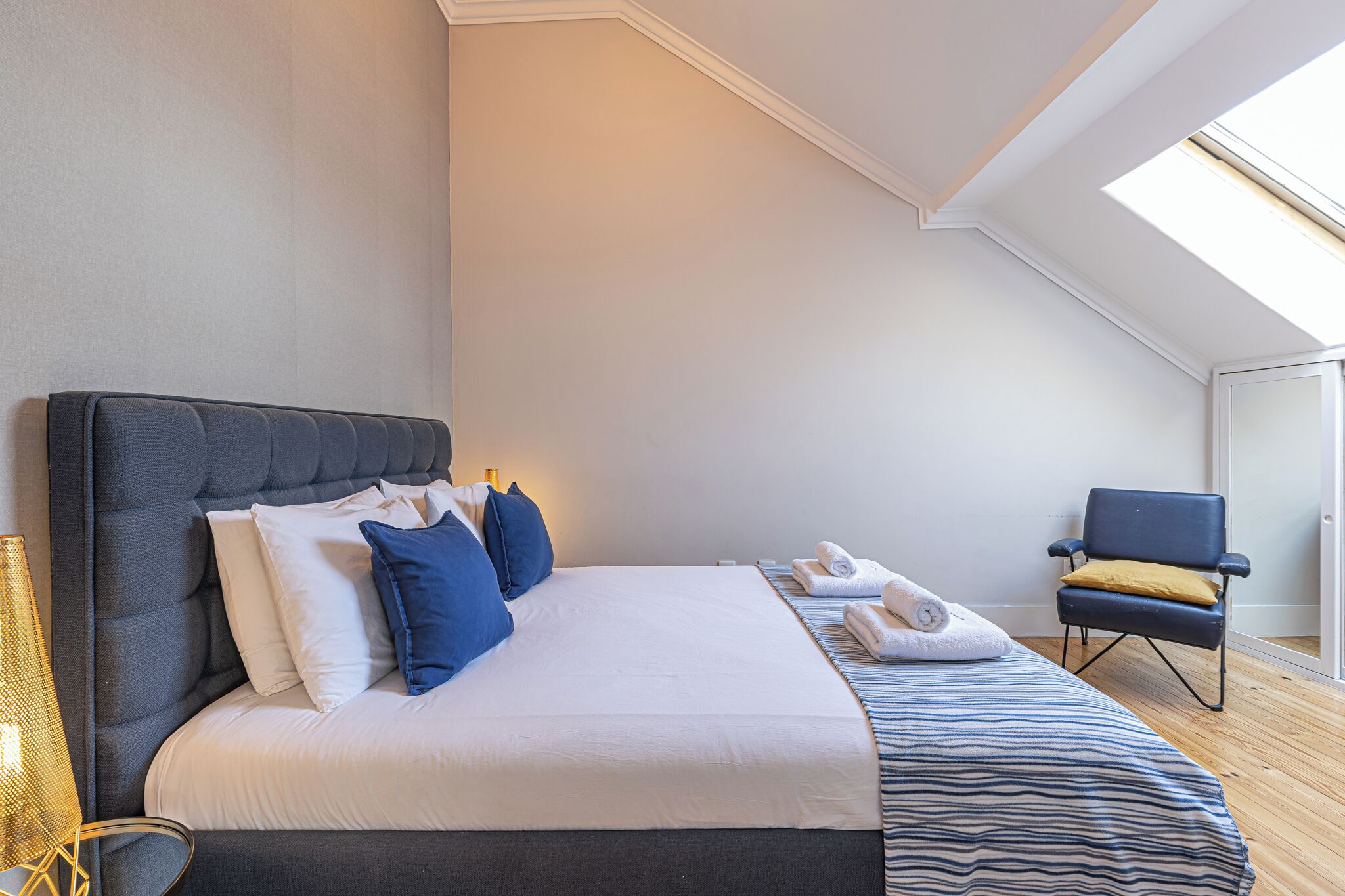 A modern hotel room with a large bed, a chair, and a skylight.