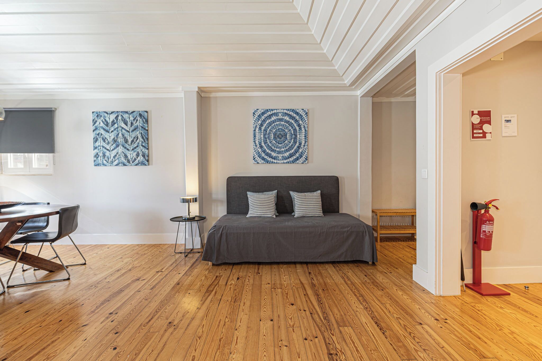 A modern bedroom with a wooden floor, a bed with grey bedding, a small bedside table, and a wall-mounted artwork.