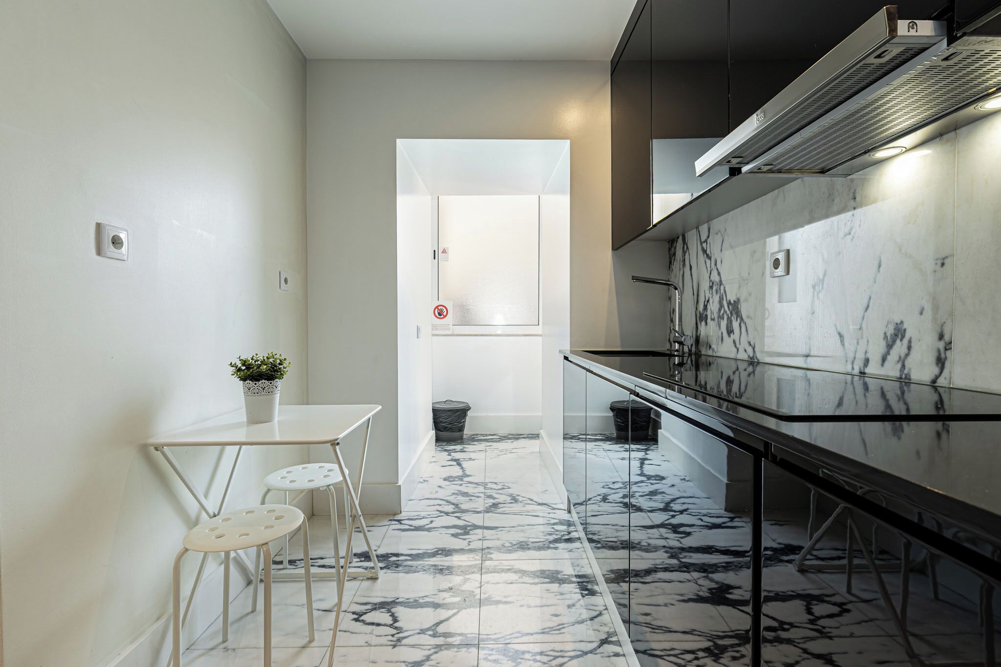 A modern kitchen with a marble backsplash, a glass dining table, and two stools.
