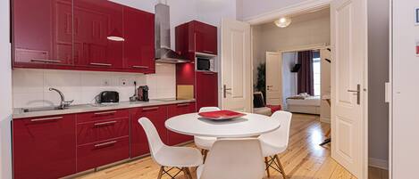 A modern kitchen with red cabinets, a white dining table with four chairs, and a wooden floor.