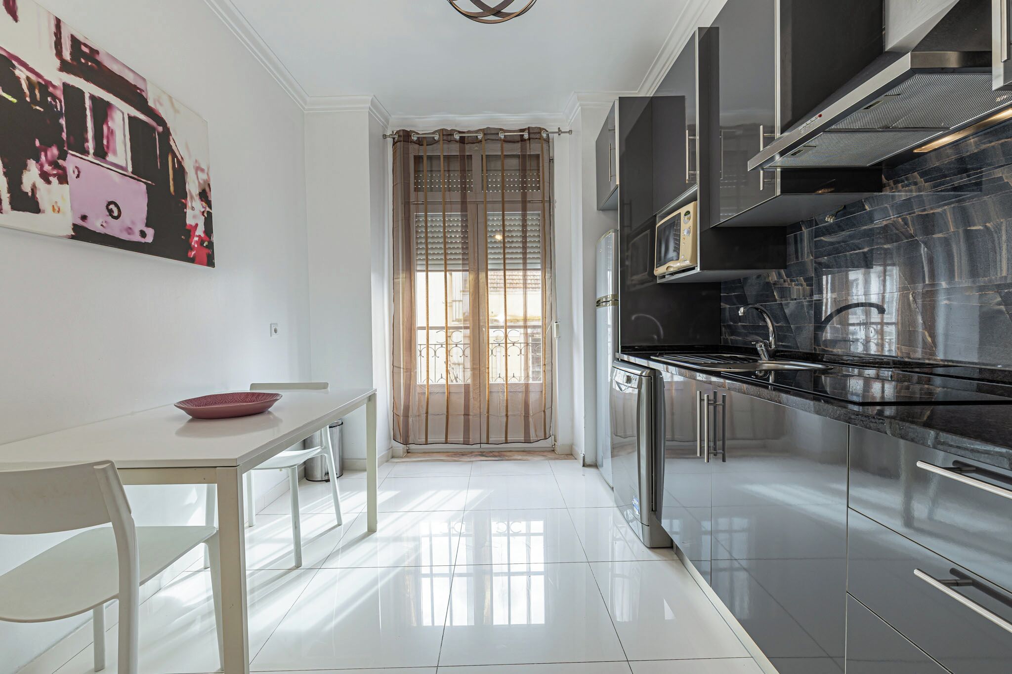 A modern kitchen with black cabinets, stainless steel appliances, and a white dining area with a table and chairs.