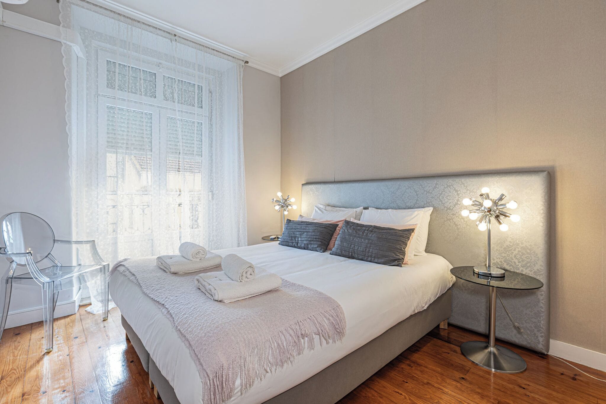 Un dormitorio con una cama grande, lámparas de noche, una silla y una ventana con cortinas.