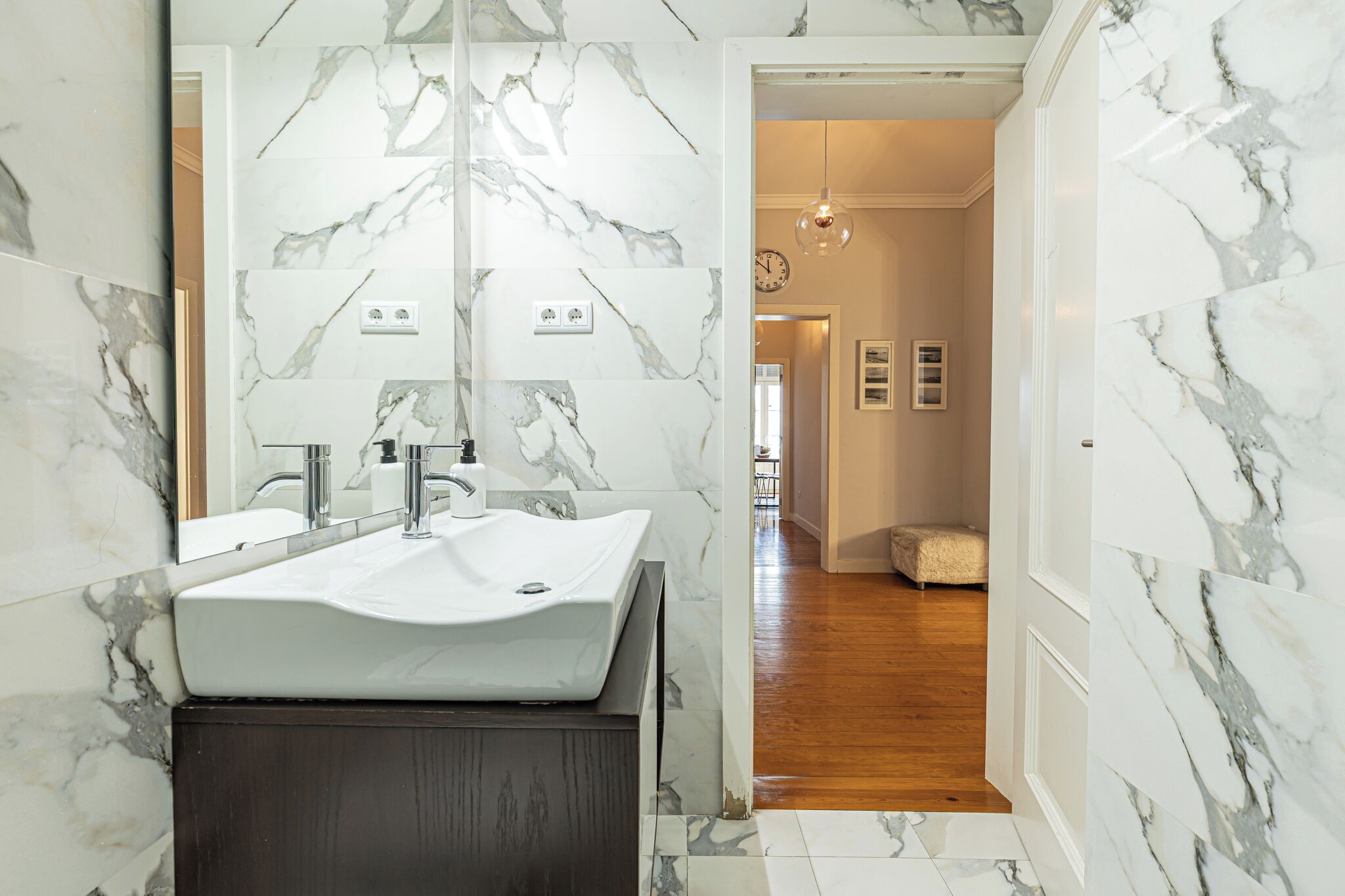 A bathroom with a marble backsplash, a white sink, and a wooden vanity.