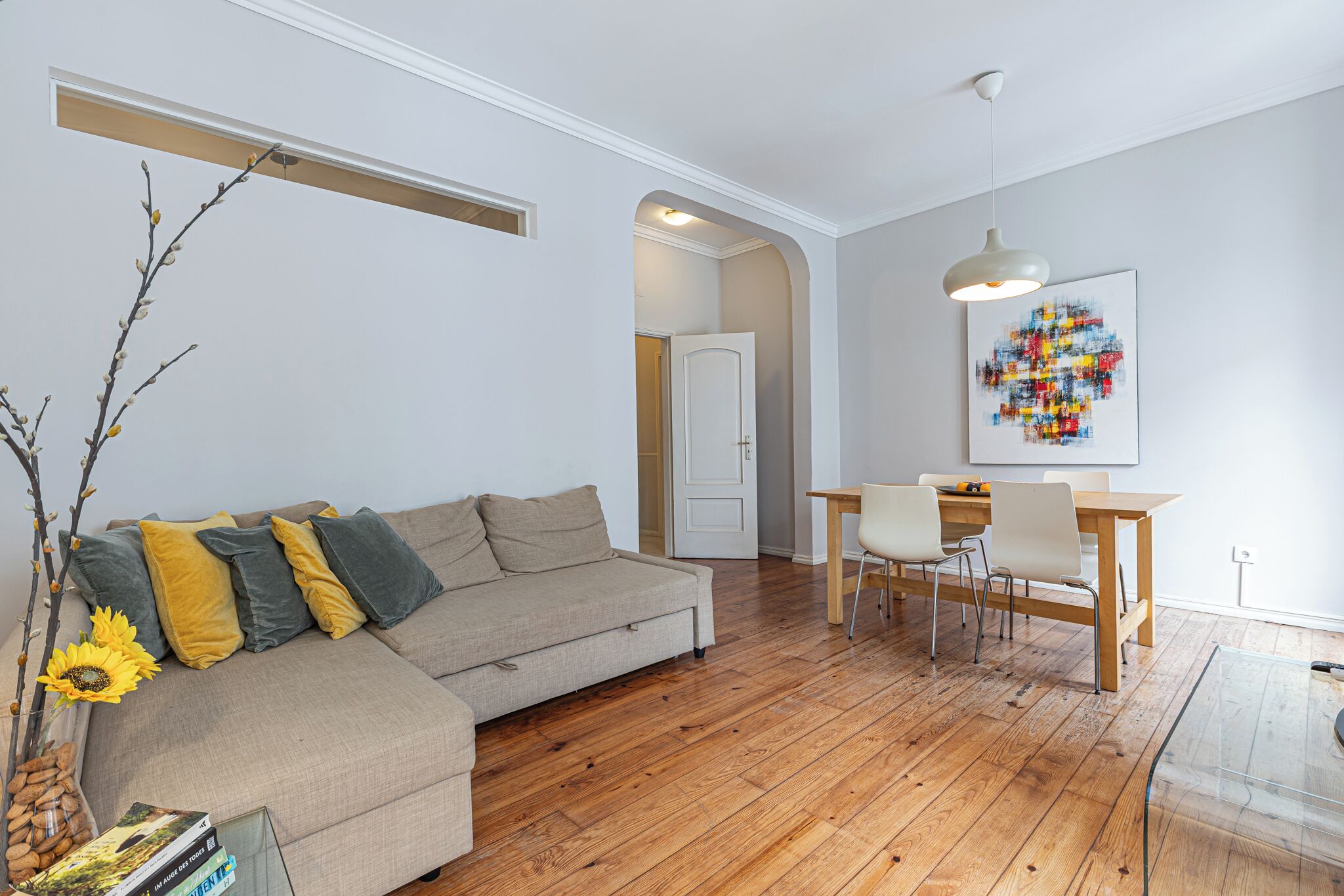 A modern living room with a sofa, a dining table with chairs, a wooden floor, and a ceiling light.