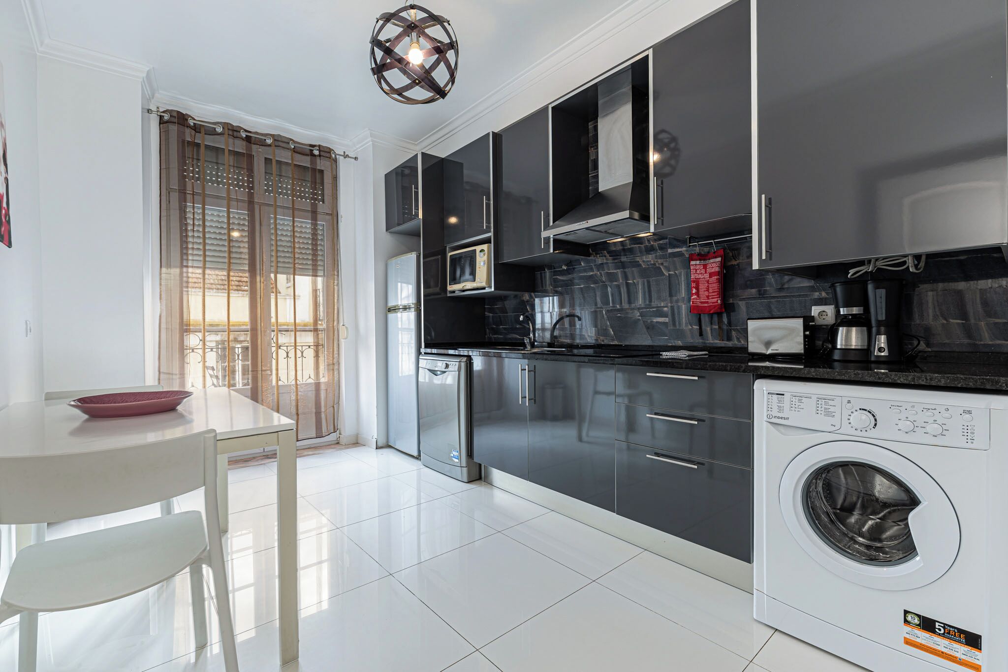 A modern kitchen with black cabinets, a white washing machine, and a dining area with a white table and chairs.