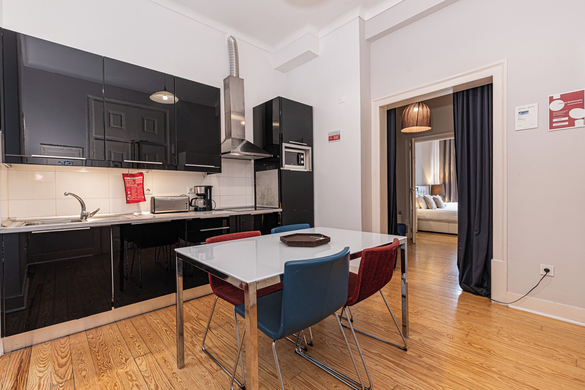 A modern kitchen with black cabinets, a white countertop, and a dining area with a white table and blue chairs.