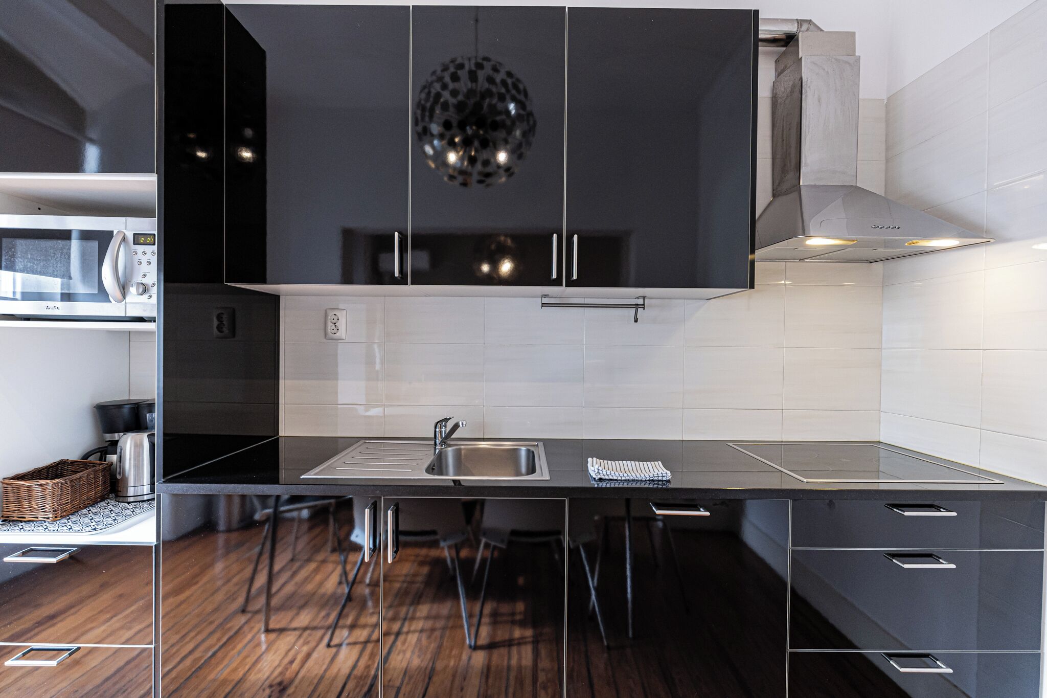 A modern kitchen with a black countertop, stainless steel sink, and a hanging spherical light fixture.