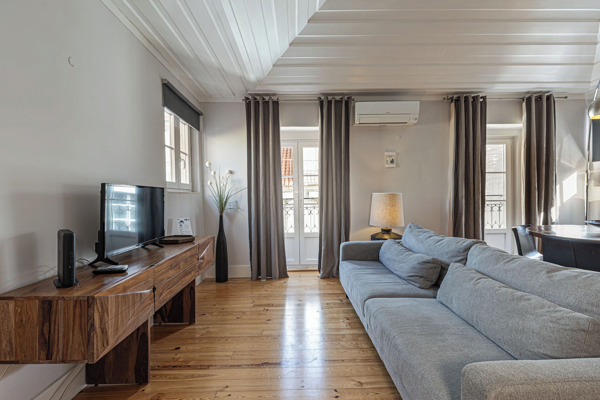 A living room with a wooden TV stand, a grey sofa, and a lamp.