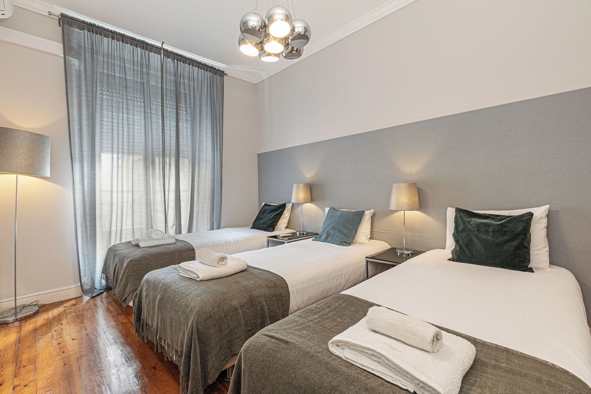 Une chambre d’hôtel avec deux lits, une grande fenêtre avec des rideaux, une lampe de sol et un lustre moderne.