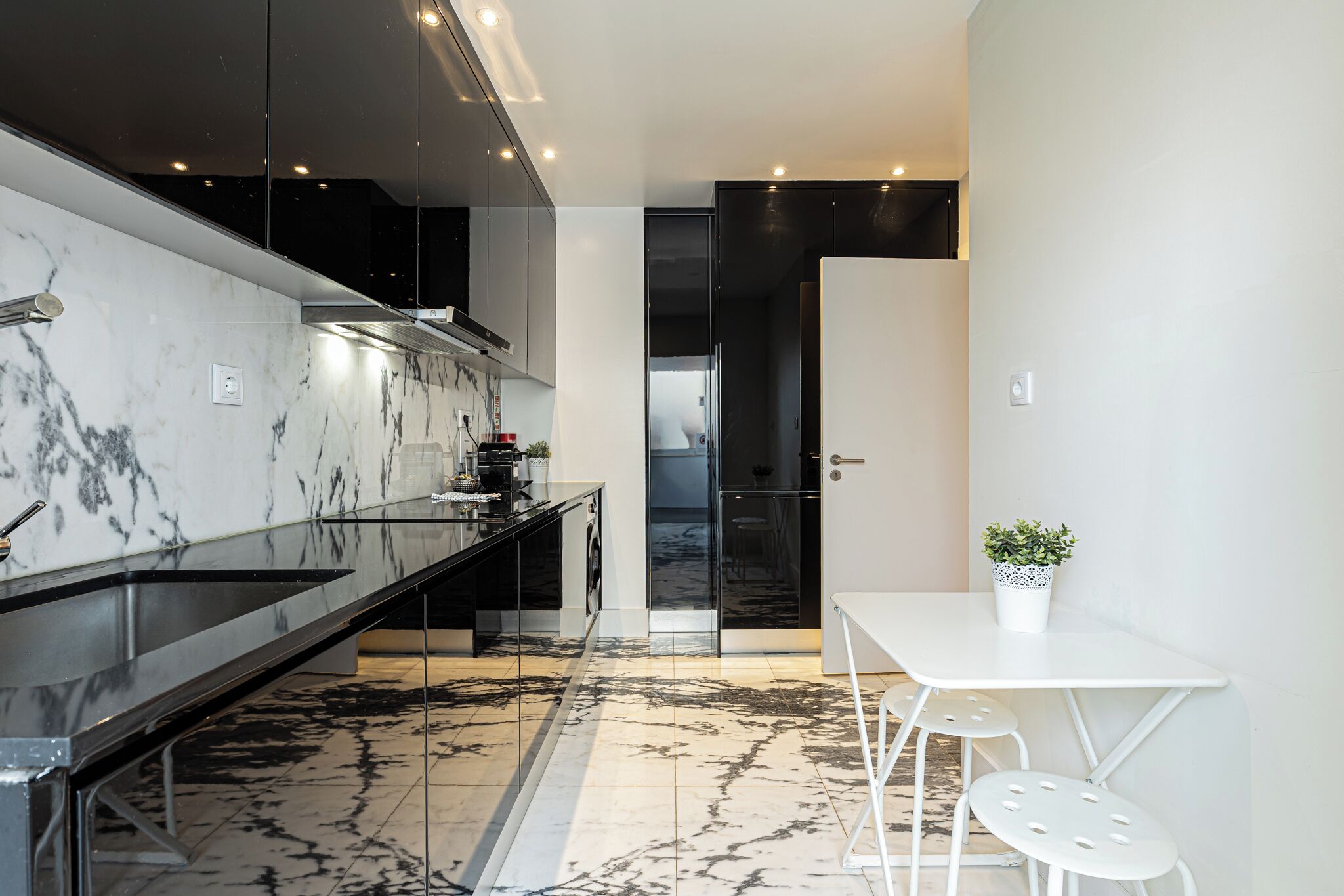 Una cucina moderna con pannelli in marmo, elettrodomestici in acciaio inossidabile e una zona pranzo bianca con sgabelli.