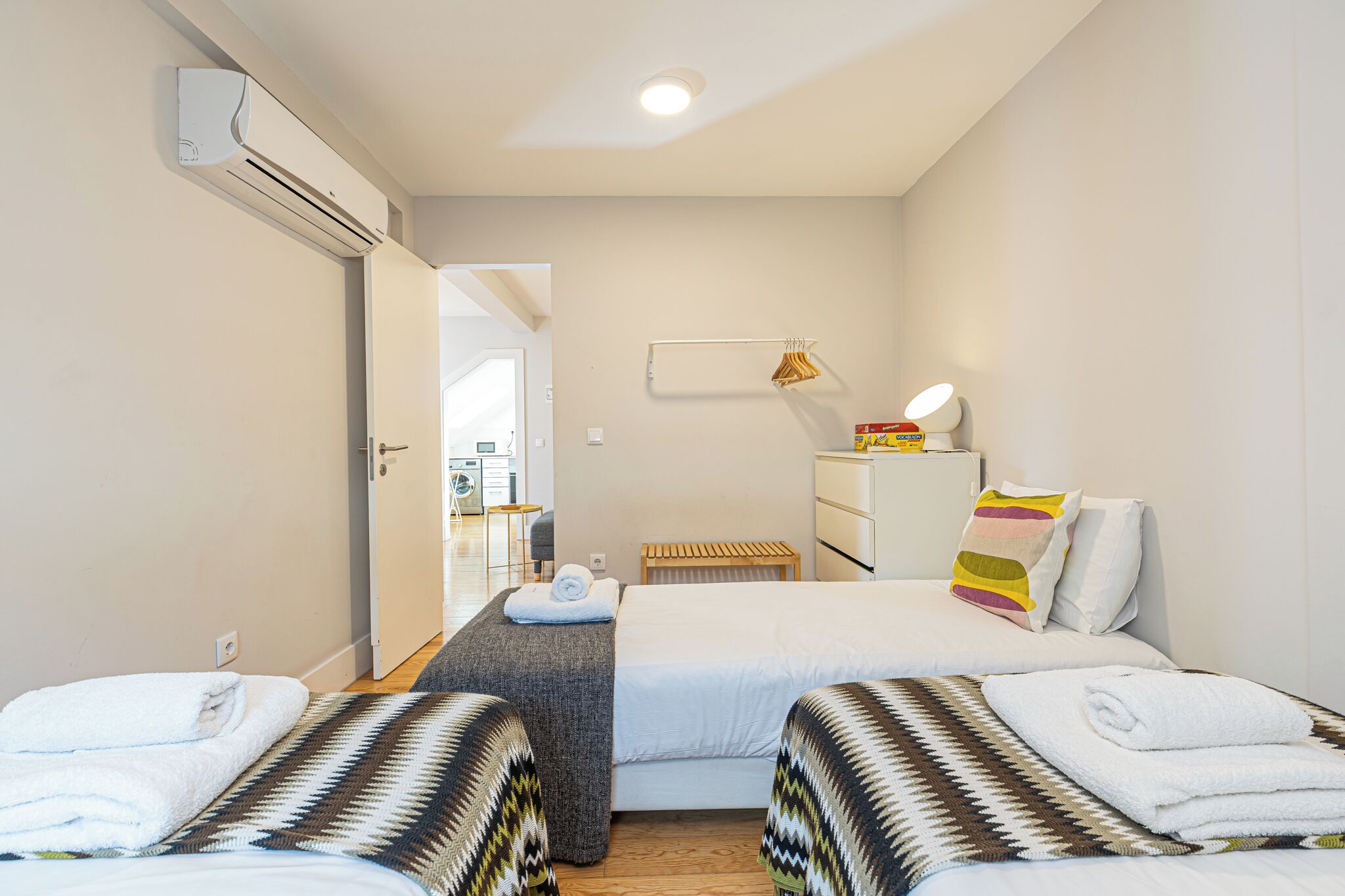 A hotel room with two beds, a desk, a chair, a lamp, and an air conditioning unit.
