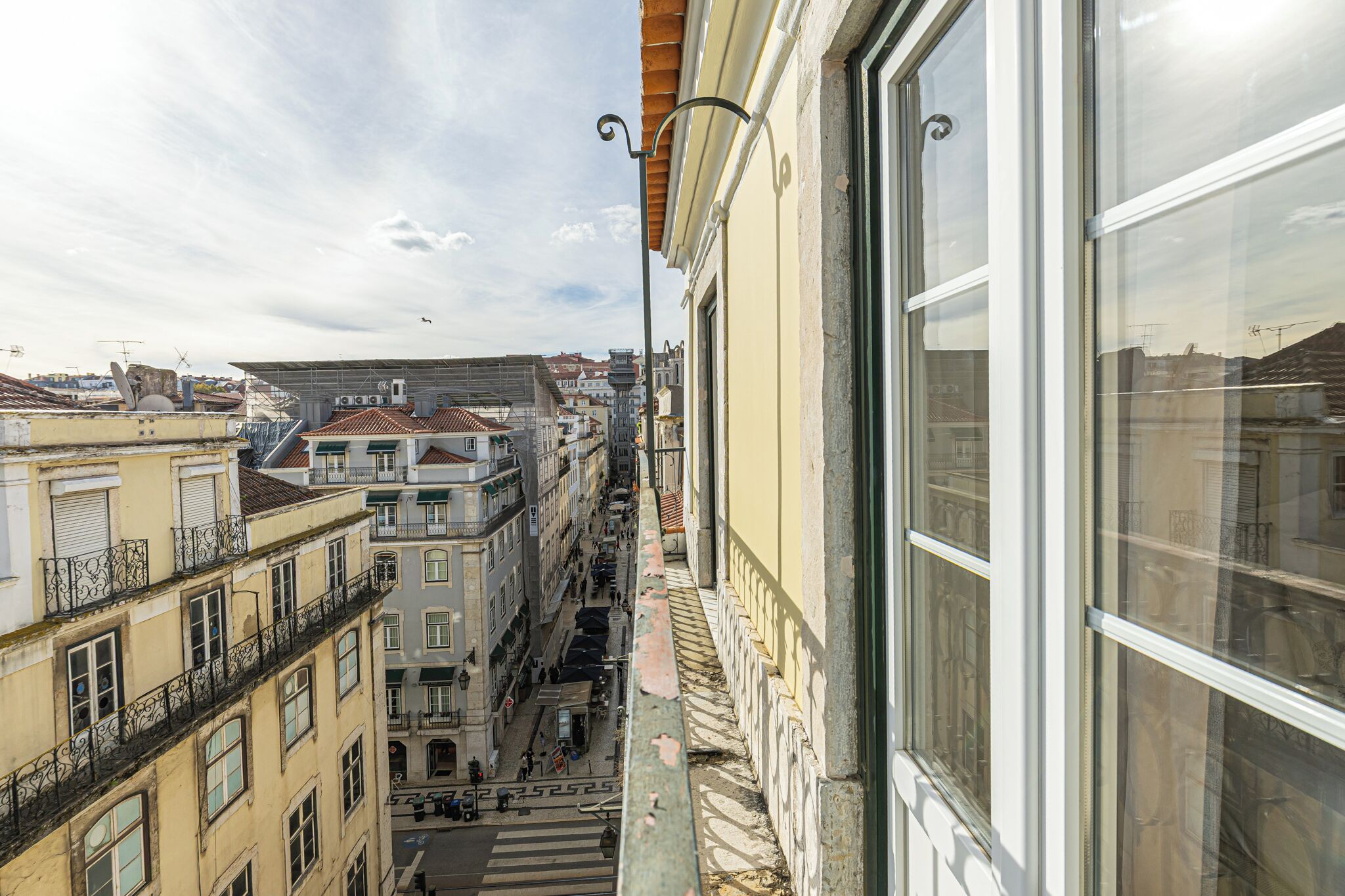 Eine schmale Straße mit Gebäuden an beiden Seiten, einer Fußgängerampel und blauem Himmel.