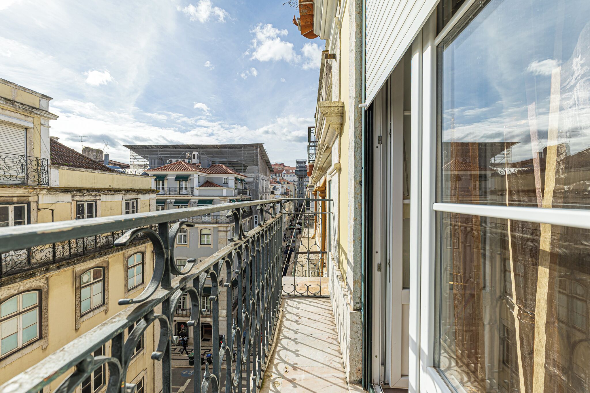 A balcony with a wrought iron railing overlooking a street with buildings.